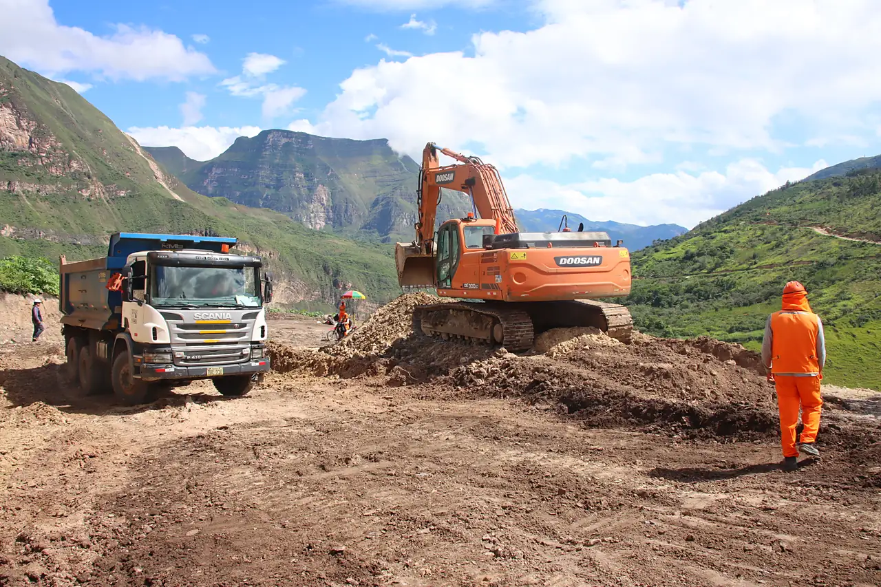Maquinaria pesada y un trabajador en una obra de movimiento de tierras en una zona andina